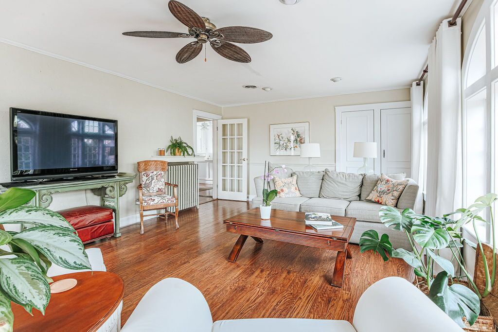 A spacious living room with a large flat-screen TV, a ceiling fan, and a wooden coffee table.