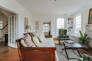 A spacious living room with a wooden sofa, a green armchair, a coffee table, and a fireplace. - The Cardinal House (Waynesboro)