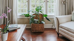 Una habitación con un amplio ventanal de arco, suelo de madera, sofá blanco y una mesa con una planta y un florero.