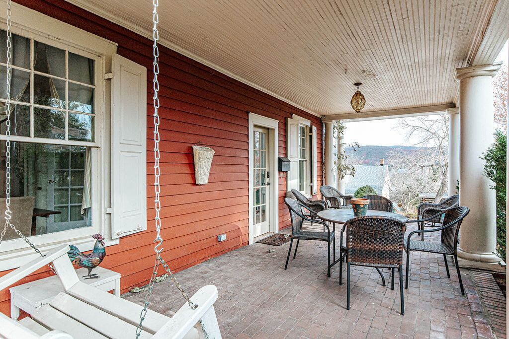 A covered porch with a swing, wicker chairs, and a table.