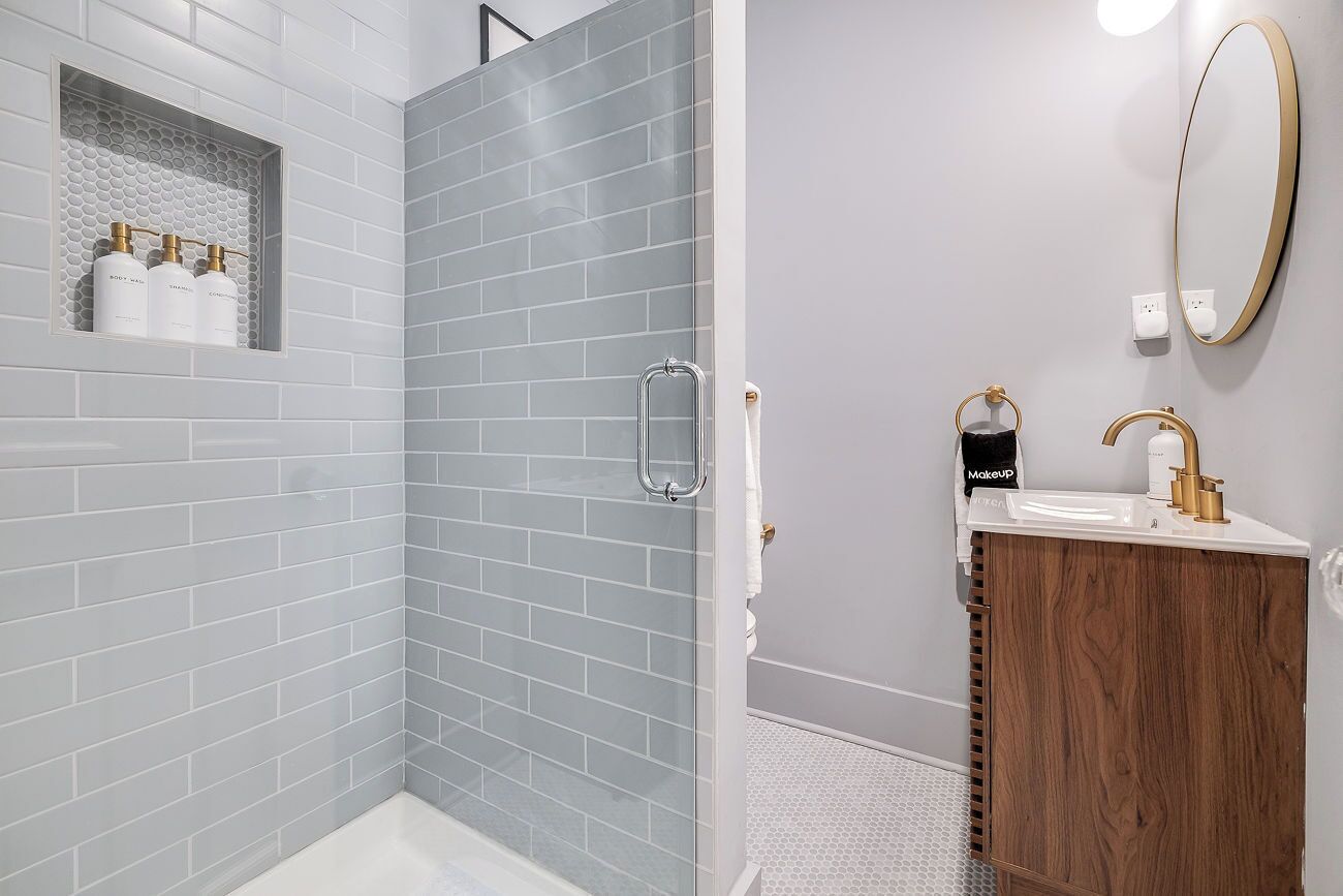Un baño moderno con ducha, tocador con espejo y repisas para artículos de aseo.