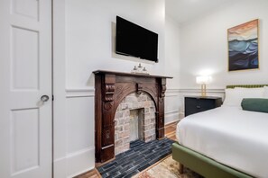 Une chambre à coucher avec une cheminée, un lit, une table de chevet, une lampe et un tableau au mur.