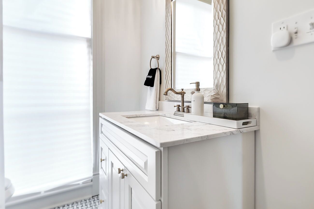 A bathroom with a white vanity, a mirror, a towel rack with a towel, and a soap dispenser.
