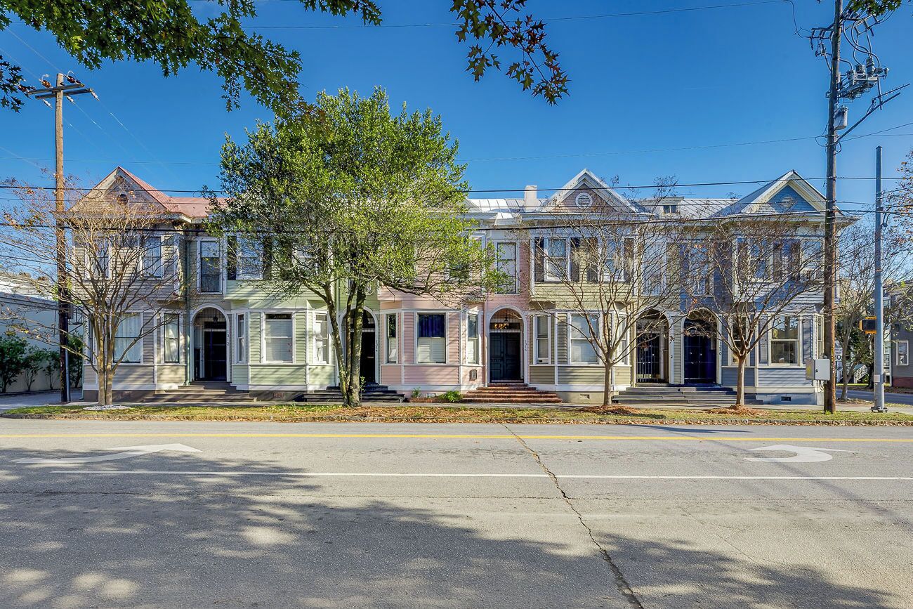 A row of Victorian-style houses with a central entrance, a driveway, and a clear sky.
