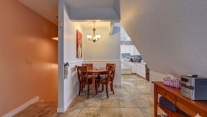 A dining area with a table and chairs, a chandelier, a kitchen in the background, and a wooden side table with a radio. - The Terrace 2 BR near the courthouse square with a King bed in the master BR (Prescott)
