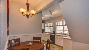 A dining area with a wooden table and chairs, a chandelier, and a kitchen with white cabinets and a window. - The Terrace 2 BR near the courthouse square with a King bed in the master BR (Prescott)