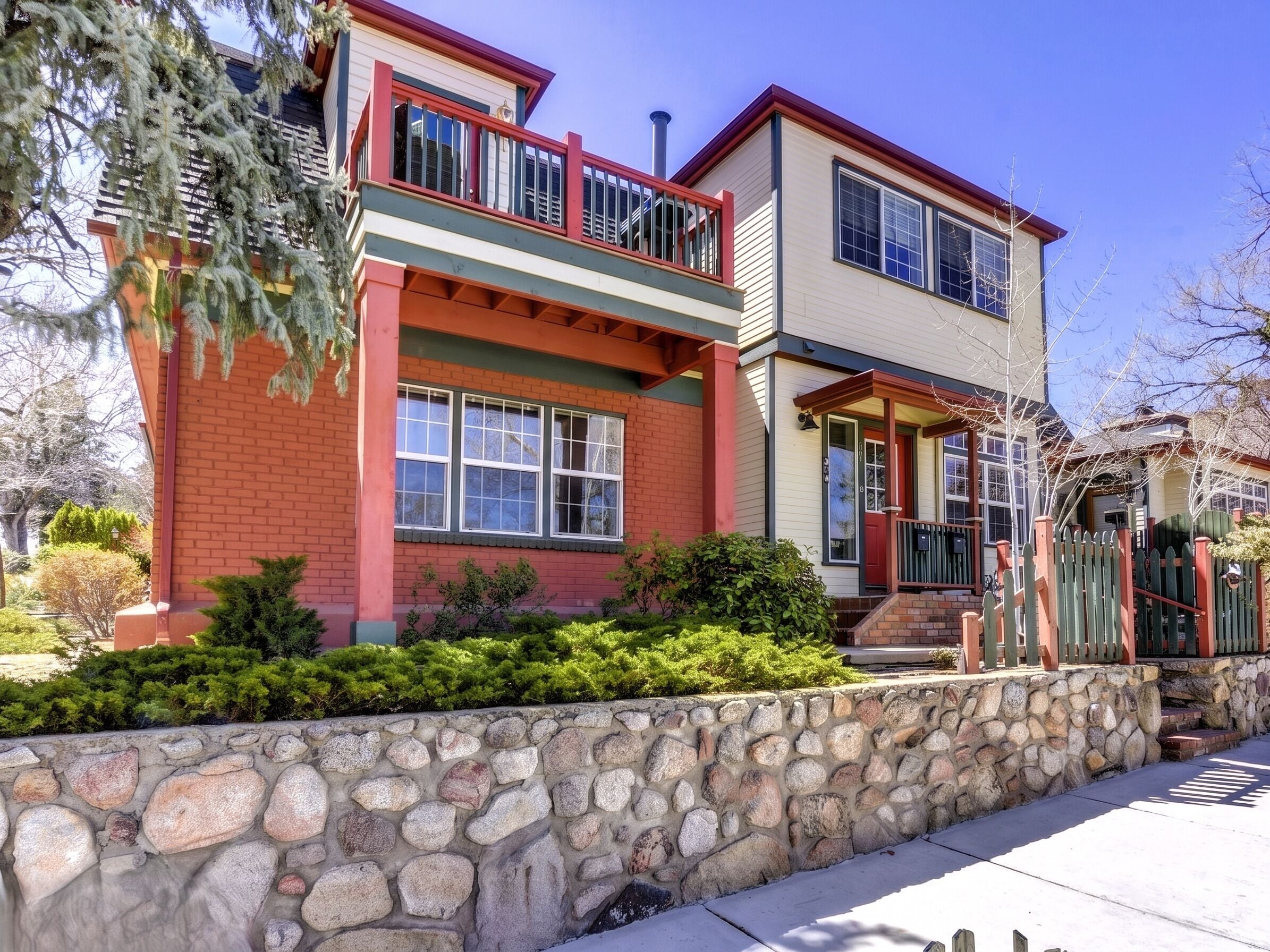A two-story house with a stone foundation, a red brick facade, and a green roof.