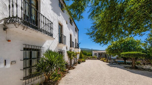A white building with balconies, a gravel path, and greenery. - Casa rural de gran capacidad (Alcala la Real)