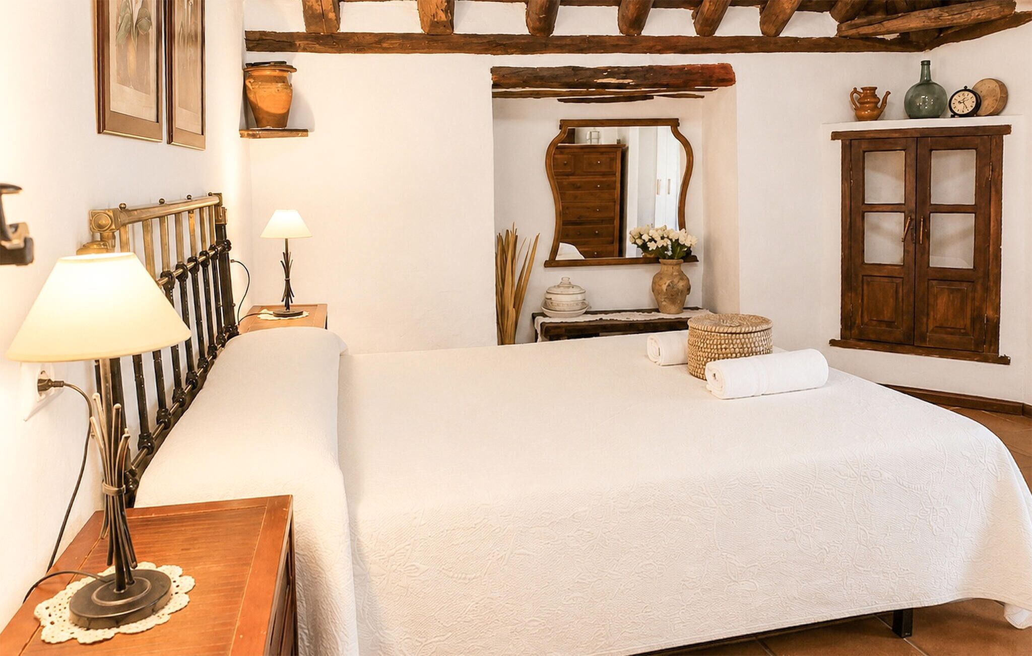 A bedroom with a bed, a nightstand, a lamp, a dresser, a mirror, and a wooden ceiling.