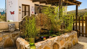 A stone planter with water and plants, a wooden fence, and a building with a door and windows. - Casa rural de gran capacidad (Alcala la Real)