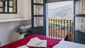 Una habitación con cama, ventana con vistas a las montañas y balcón con barandilla.