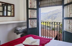 Ein Zimmer mit einem Bett, einem Fenster mit Bergblick und einem Balkon mit Geländer.