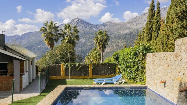 Piscina con vista a la montaña, un muro de piedra y un área cercada con una silla de descanso.