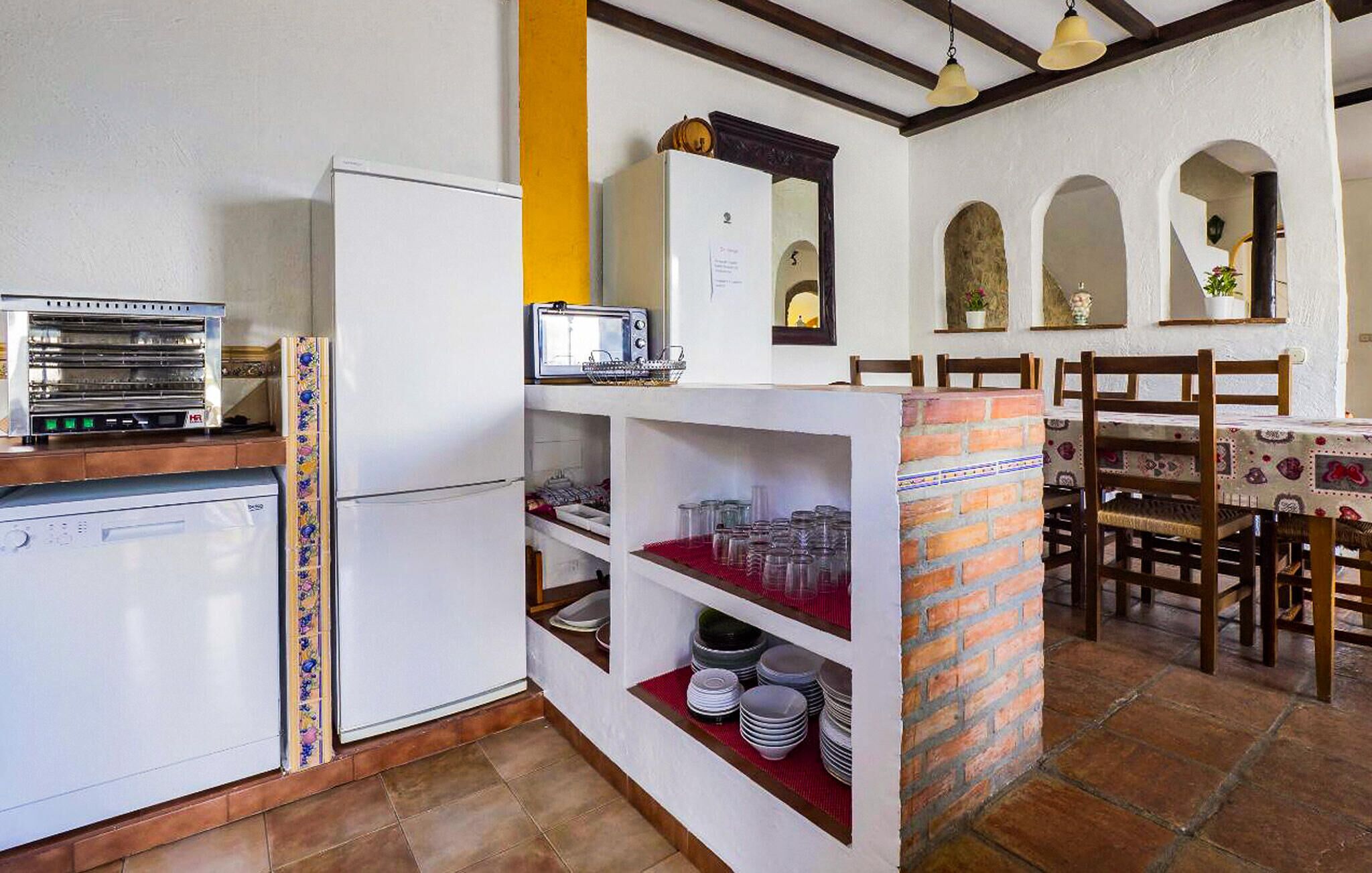 A compact kitchen with a refrigerator, a microwave, and a toaster. There are shelves with dishes and a brick accent wall.