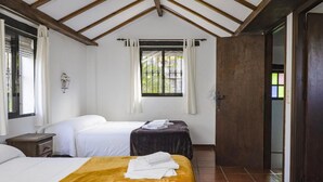 Una habitación con dos camas, una ventana con cortinas, techo de madera y una puerta que da a otra habitación.