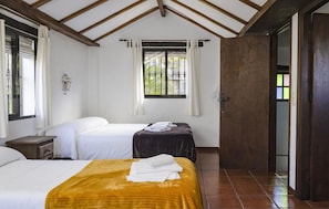 Ein Zimmer mit zwei Betten, einem fensterbelaubten Fenster, einer Holzzahlende Decke und einer Tür zu einem weiteren Zimmer.