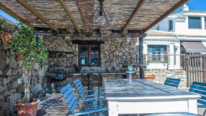 A covered outdoor seating area with stone walls, a stone fireplace, and a table with chairs.