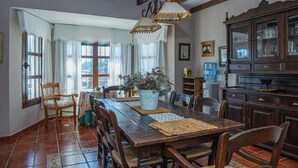 A dining area with a wooden table, chairs, a vase with flowers, and a cabinet with glassware.