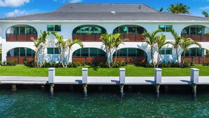 A modern two-story house with a waterfront view, featuring a deck and palm trees.