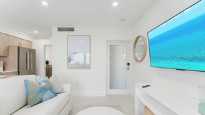 A modern living room with a white sofa, a flat-screen TV, and a large window overlooking a body of water.