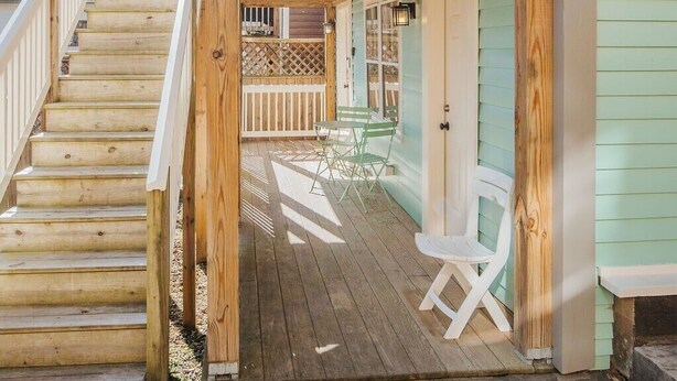 Une terrasse en bois avec un escalier menant à une zone couverte, un petit espace extérieur aménagé avec des chaises, et une vue sur une maison en arrière-plan.