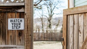 Une porte en bois sur laquelle est affiché un panneau indiquant : « FAITES ATTENTION OÙ VOUS METTEZ LES PIEDS ».