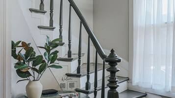 A staircase with black balusters and a chandelier, a round table with a vase and a QR code, and a window with sheer curtains.