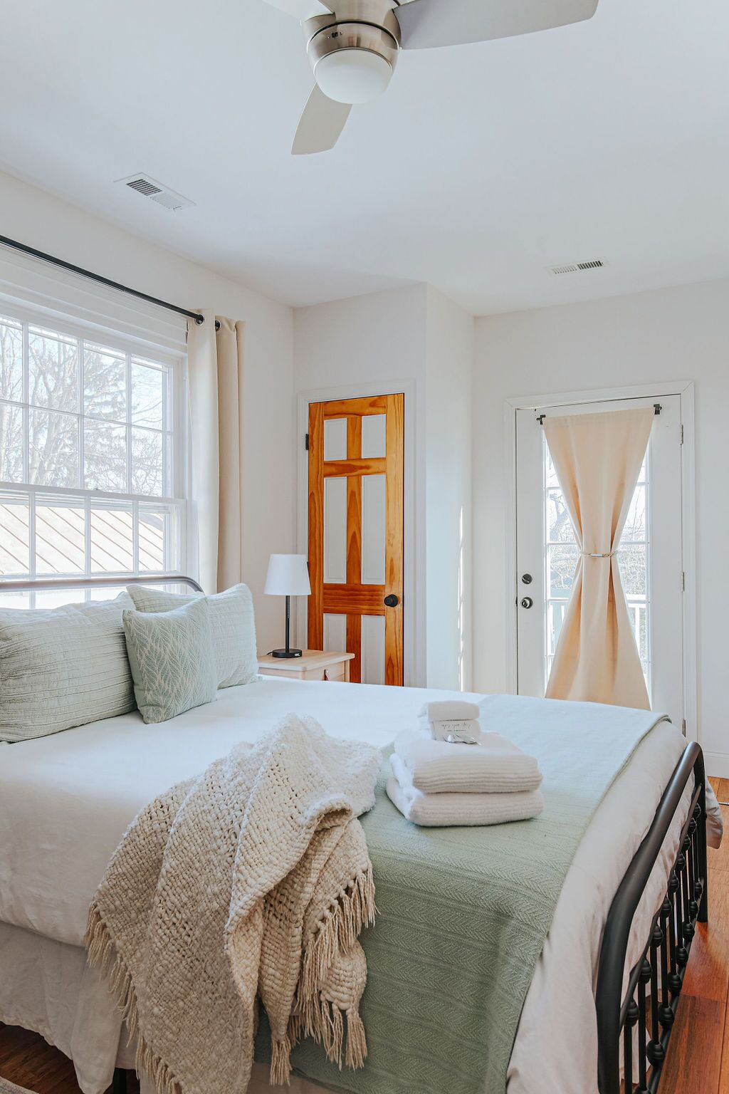 A bedroom with a bed, a ceiling fan, a wooden door, and a window with curtains.