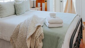 Quarto com cama, ventoinha no teto, porta de madeira e janela com cortinas.