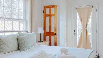A bedroom with a bed, a ceiling fan, a wooden door, and a window with curtains.
