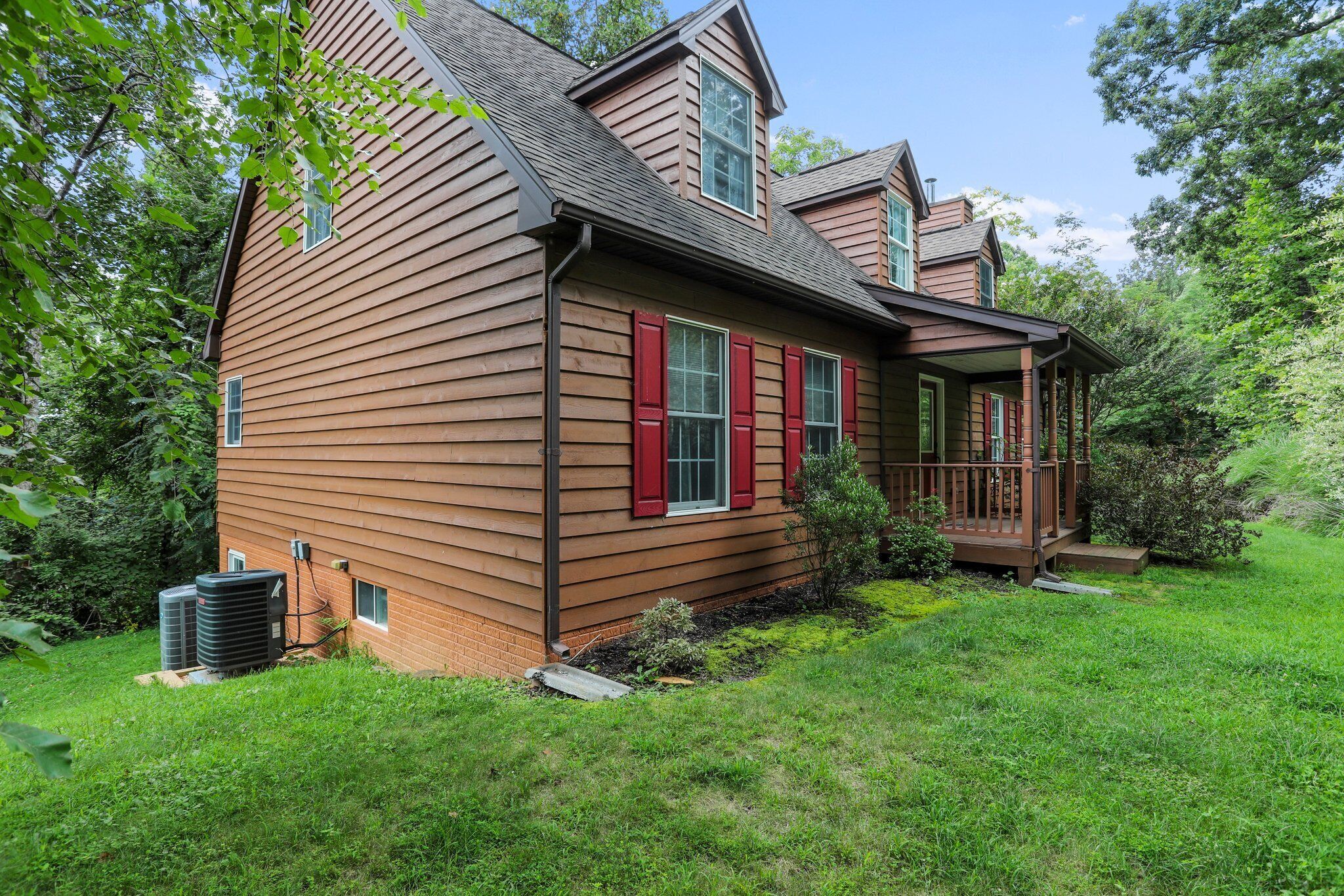 A two-story wooden house with a covered porch, a small garden, and an air conditioning unit.