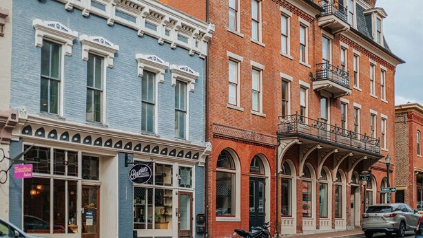 A row of multi-story buildings with commercial storefronts, including a visible sign for a restaurant. - The Social Loft (Staunton)