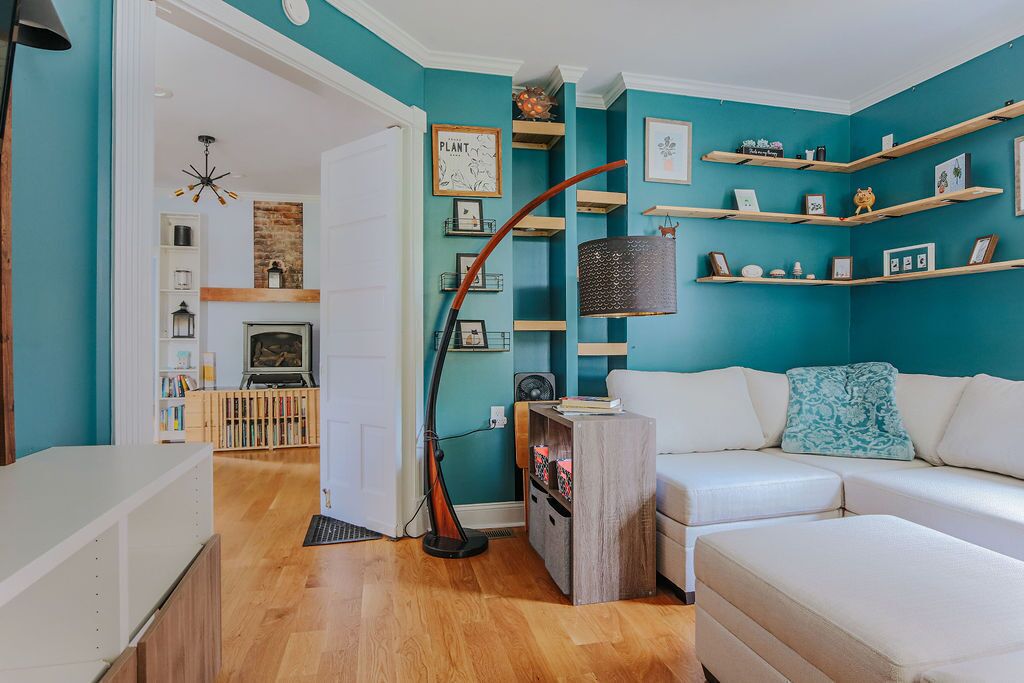 Un soggiorno moderno con pareti color petrolio, un divano bianco, scaffali in legno e un camino.