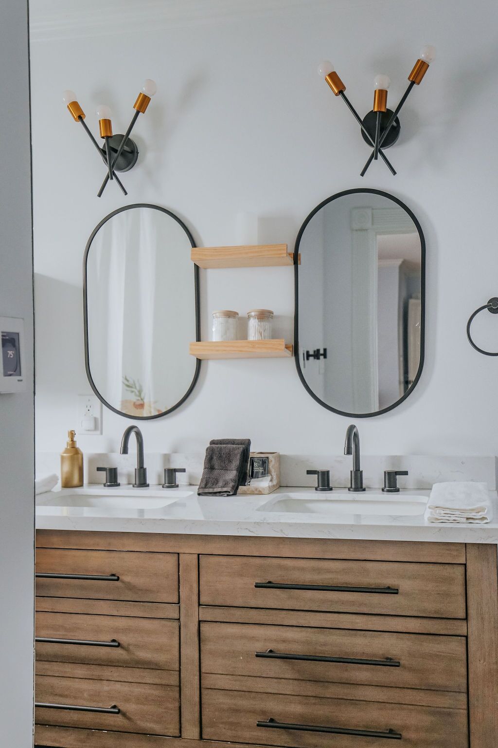 Une salle de bain avec deux miroirs ovales, un lavabo avec un robinet et des meubles en bois en dessous.
