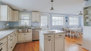 A kitchen with white cabinets, a granite countertop, a sink, and a dining area with white chairs. - The Wayne Shire (Waynesboro)