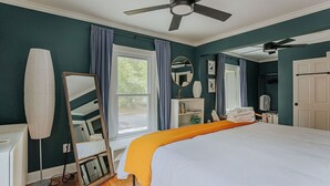 A bedroom with a bed, ceiling fan, large windows with curtains, a mirror, and a bedside table. - The Wayne Shire (Waynesboro)