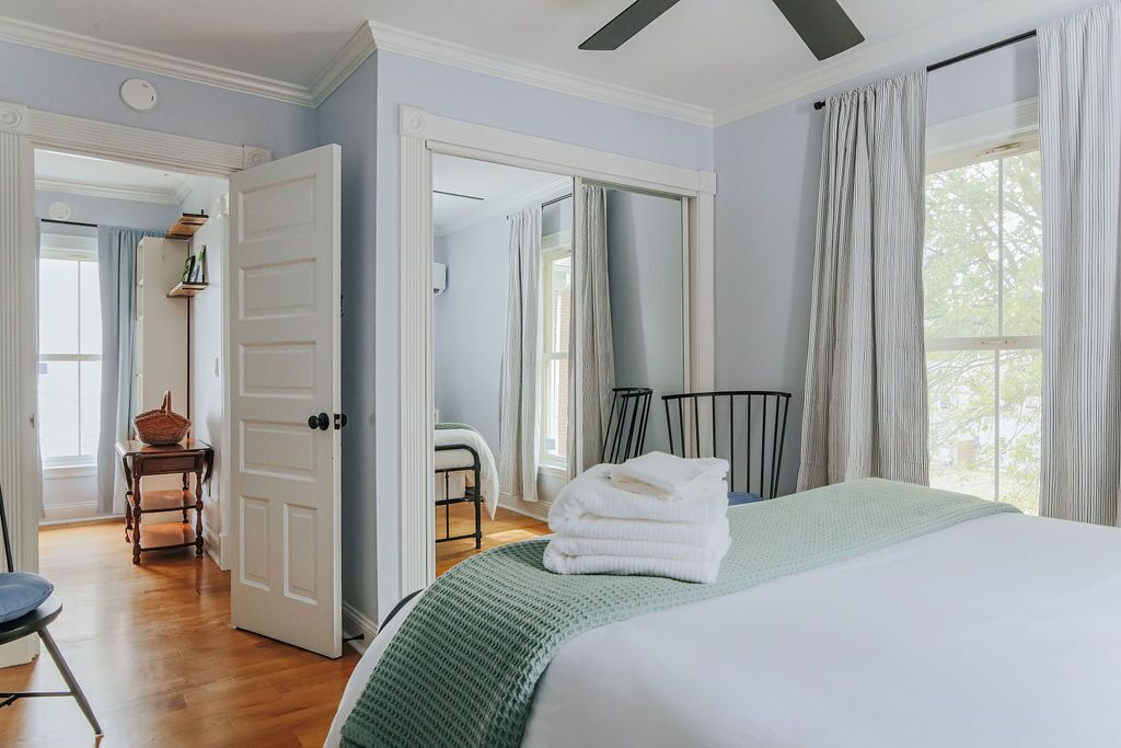 A bedroom with a bed, a chair, a table, and a door leading to another room.