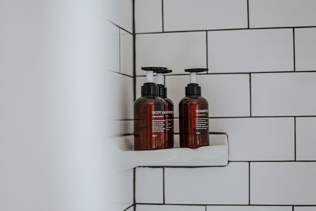 Two brown bottles of body lotion and shampoo on a white tiled shelf in a bathroom.