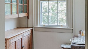 Ein Eckzimmer mit großem Fenster, Holzausstattung und einem kleinen Tisch mit Gläsern.