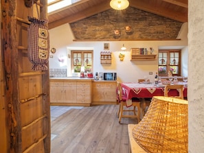 A rustic kitchen with wooden cabinets, a stone wall, and a dining area with a red tablecloth. - Chalet Ralon by Interhome (Bormio)