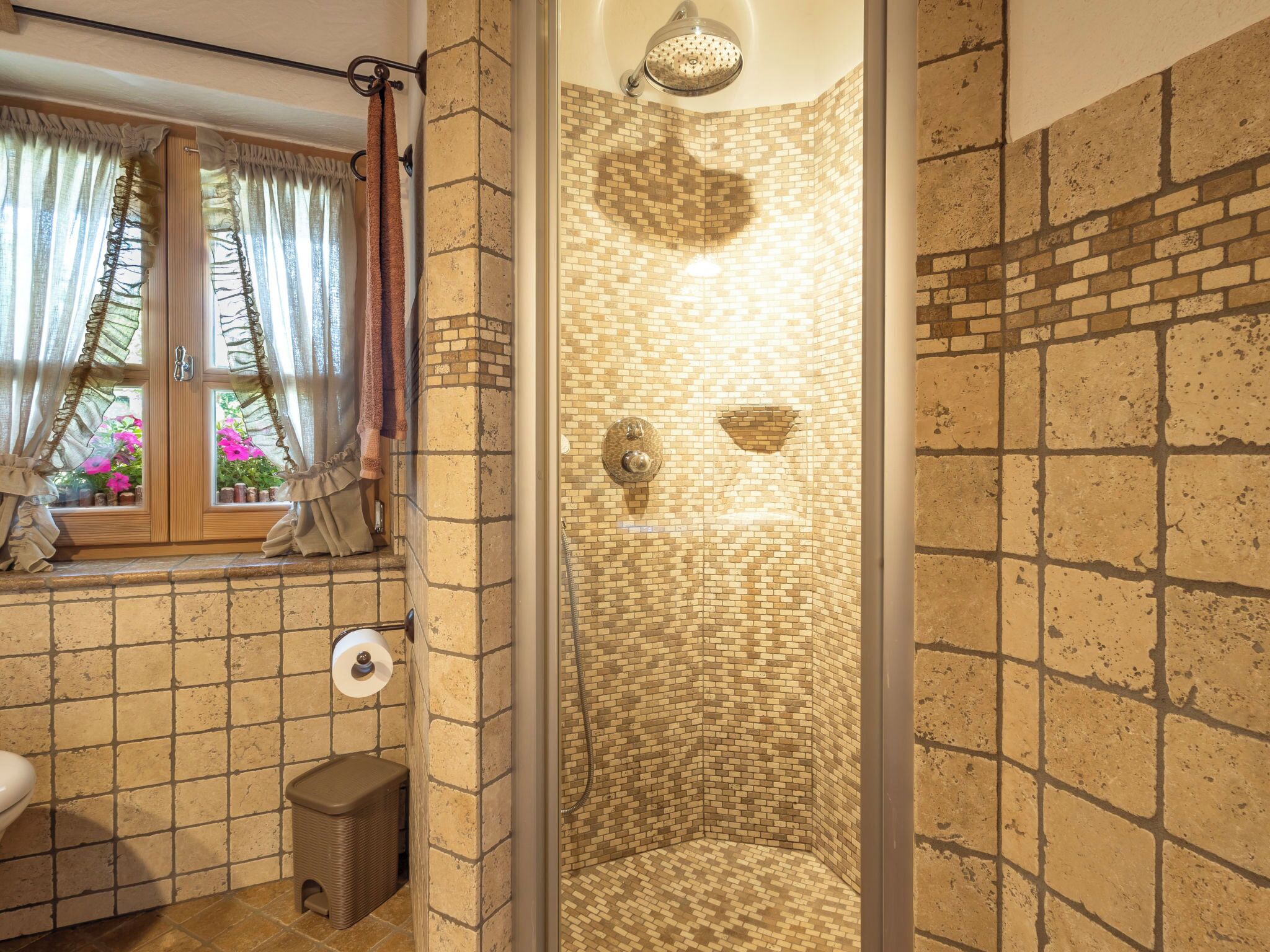 A bathroom with a shower, a window with curtains, and a toilet.