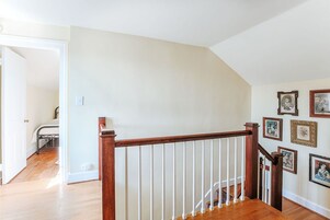 Una escalera con barandillas de madera y balaustres blancos que conduce a una habitación con cama y escritorio.