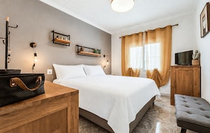 Ein Schlafzimmer mit Bett, Nachttischen, einem Fernseher und einem Fenster mit Vorhängen.