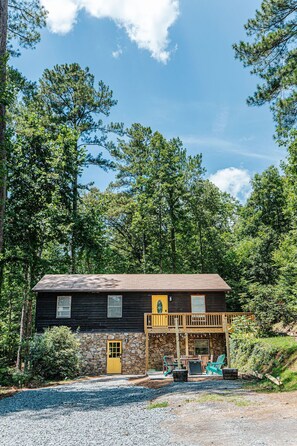 A cabin with a stone foundation, a wooden deck, and a yellow door. - Tucked Inn: Lower Unit (Nellysford)