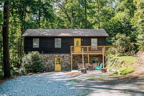 Une cabane avec des fondations en pierre, une terrasse en bois et une allée gravillonnée.