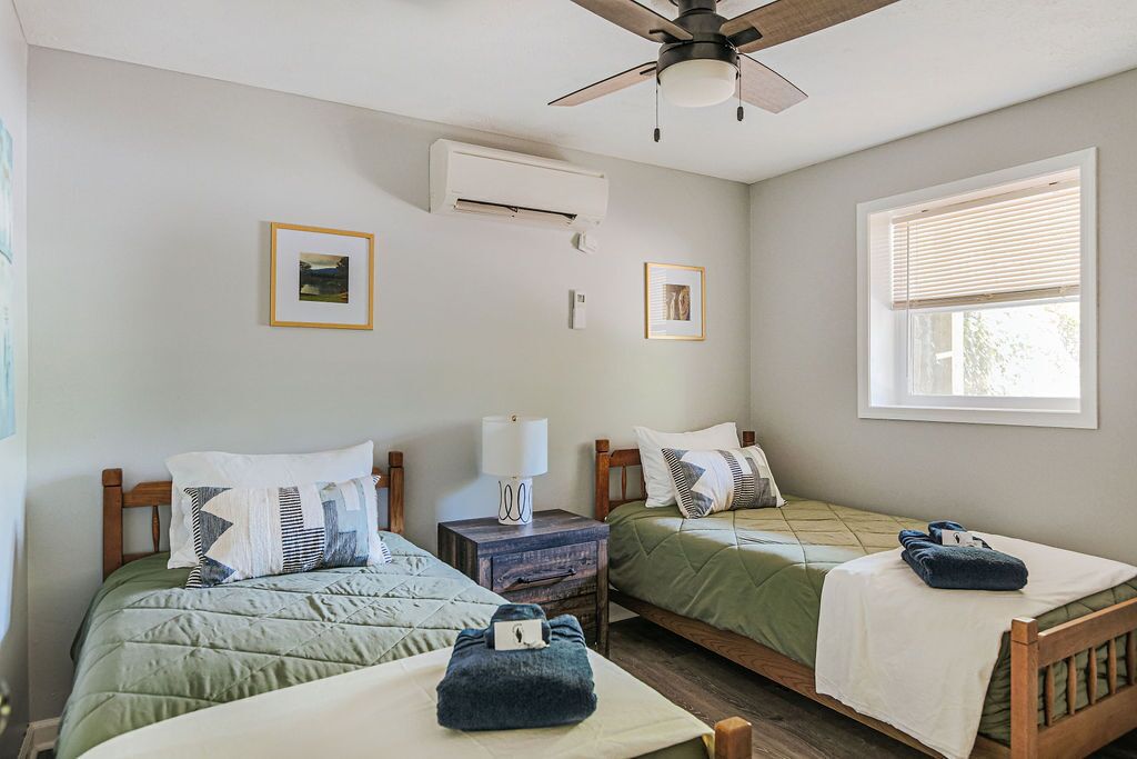 Una habitación con dos camas, ventilador de techo, aire acondicionado y una ventana con persianas.