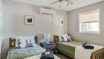 Una habitación con dos camas, ventilador de techo, aire acondicionado y una ventana con persianas.
