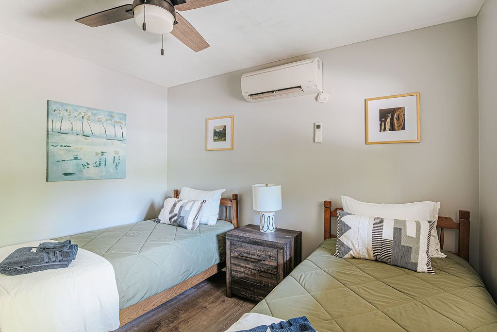 A hotel room with two beds, a ceiling fan, an air conditioning unit, and framed pictures on the walls.