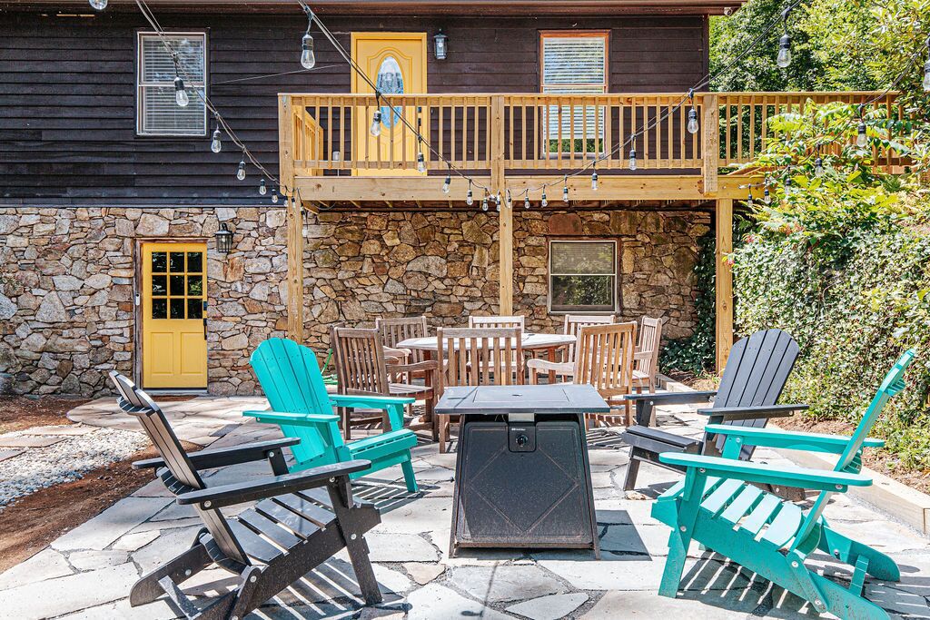 An outdoor patio with Adirondack chairs, a table, and a stone wall.
