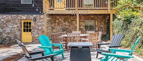 An outdoor patio with Adirondack chairs, a table, and a stone wall.